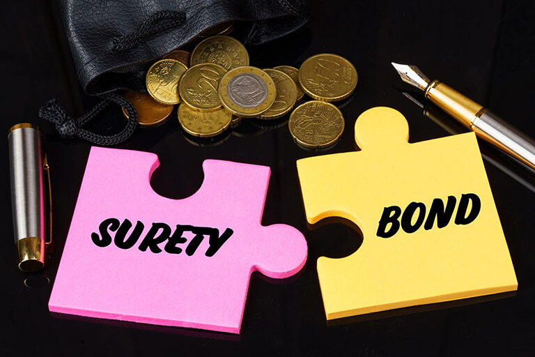  Puzzle pieces with the words “surety” and “bond” amidst coins