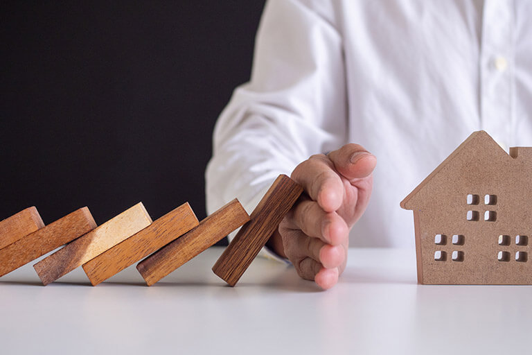  A hand protecting a house cut-out from toppling building blocks, representing the protection that surety bonds offer
