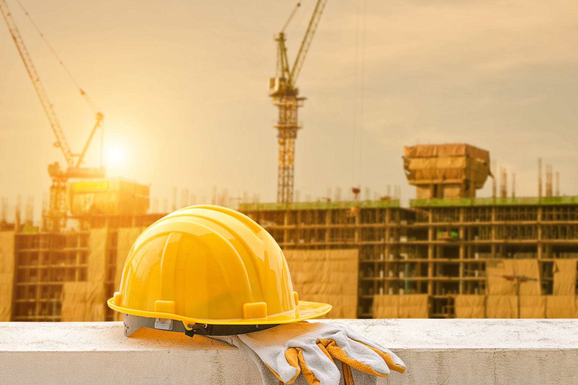 A hard hat and gloves on top of a bench, with an unfinished building in the background