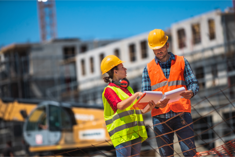 two construction site managers review plans on a clipboard
