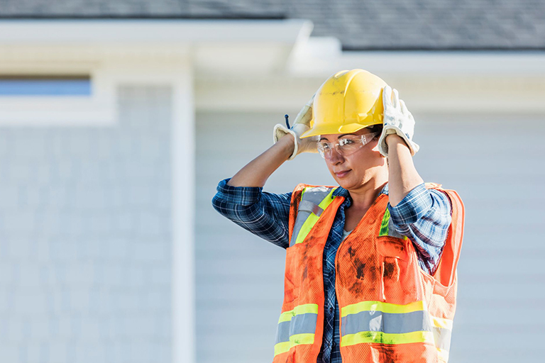 A contractor holding their hard hat in place on their head