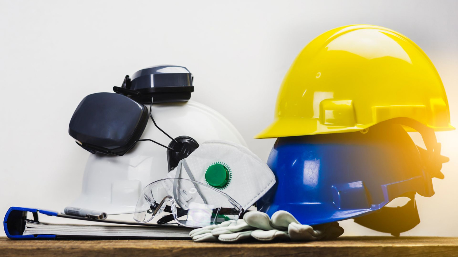 Hard hats, ear protection, gloves, and safety goggles resting on top of a wooden table