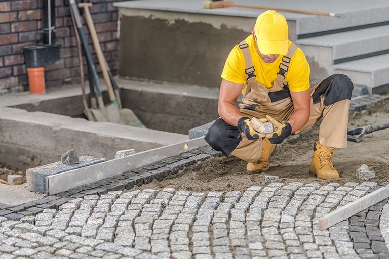 A masonry contractor sets a stone walkway with concrete