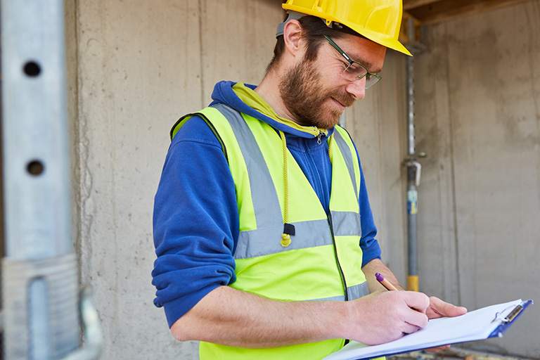 A contractor writing on paper attached to a clipboard