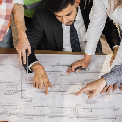 Group of Architects around a blue print pointing at a specific portion of the design